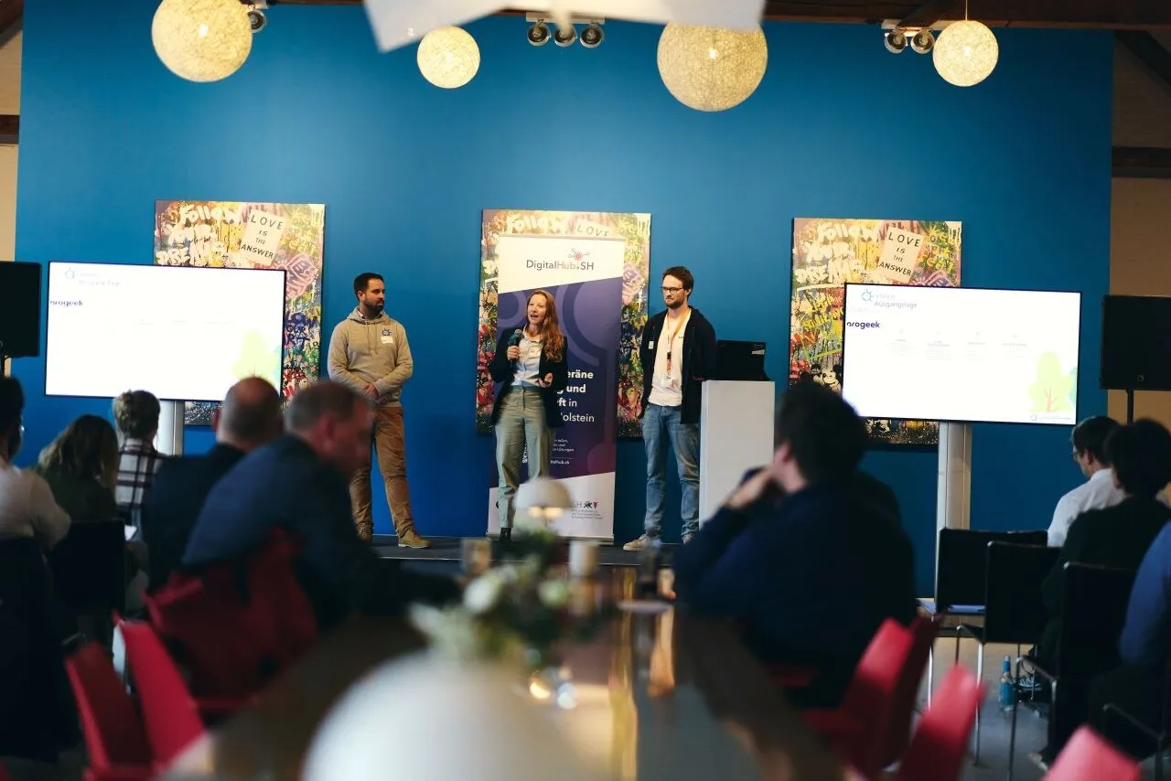 Three people present Green Ecolution on a stage, between two screens stands a DigitalHub.SH banner